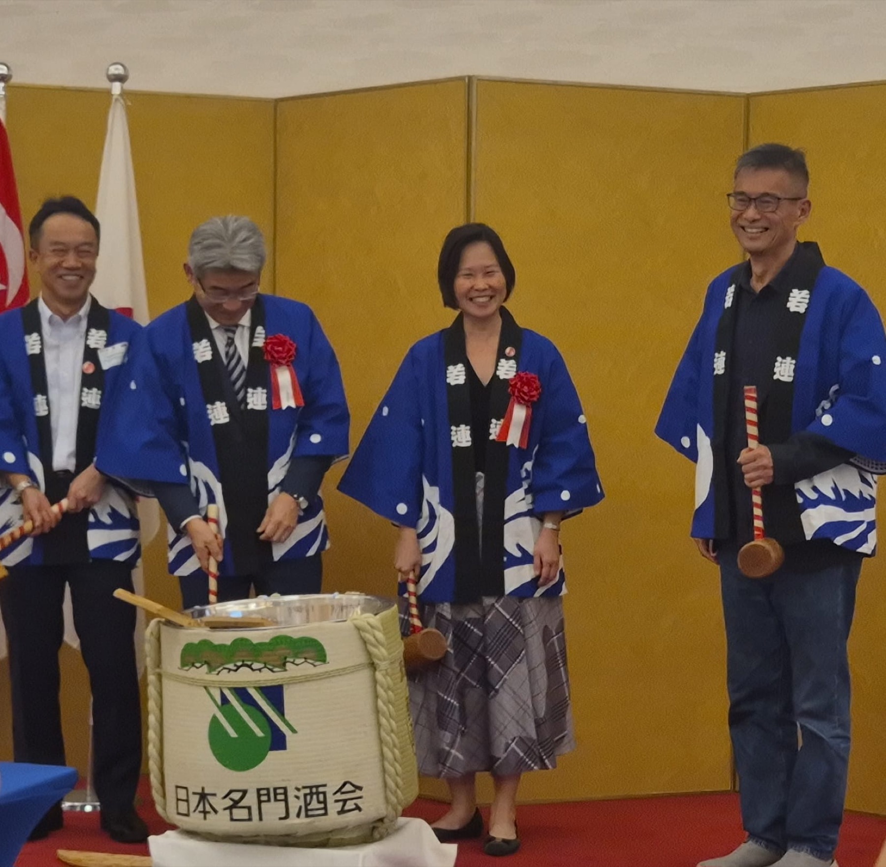 Four guests in ceremonial happi coats opening a sake barrel at a cross chamber reception